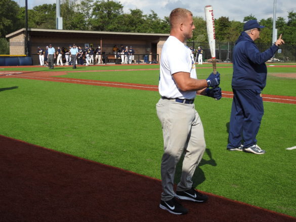 Male standing on the baseball field holding a baseball bat.