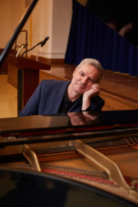 Man looking whimsical seated at the piano before playing Chopin.