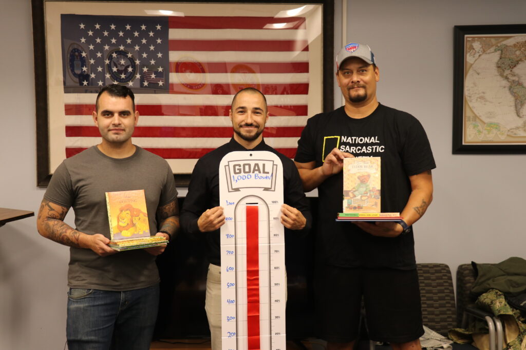 Center is John Davis holding the sign saying they reached the goal for 1,000 books, surrounded by members of SVA holding books for Cambodia.