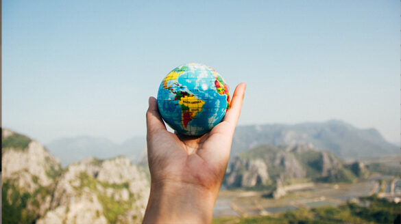 Stock photo of a person holding a small globe while looking out over an expansive view, symbolic of Earth Week.